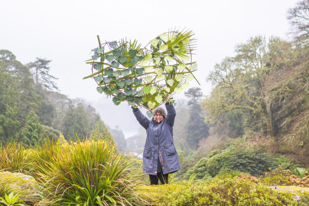 person holding up a giant heart-shape made of branches