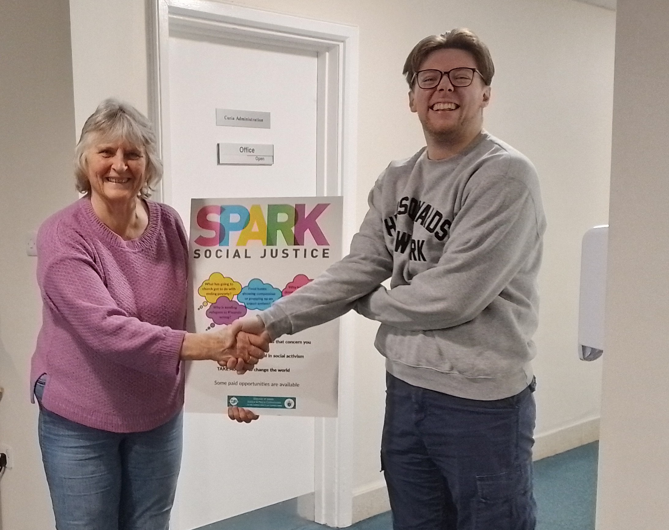 Tom and Marg shaking hands with Spark social justice poster